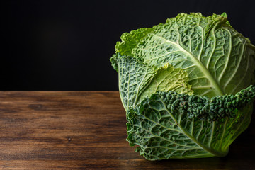 Close-up of whole curly cabbage on dark wooden board, black background, horizontal with copy space