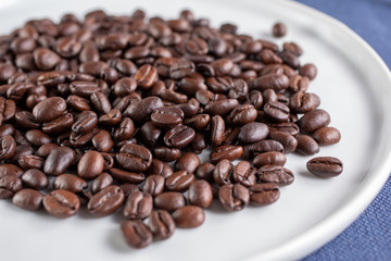 A side view of a mound of roasted coffee beans on a white place.