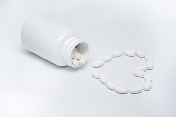 White round tablets in the shape of a heart lie in a white jar and are scattered around