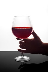 A woman's hand holds a glass of red wine on a white background.