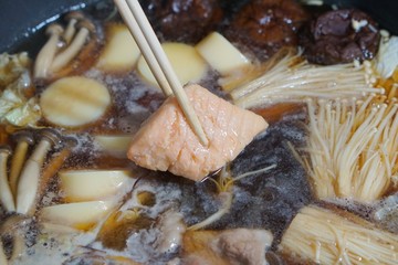 close up picture of boiled Japanese hot pot  with salmon which be grabbed with chopsticks