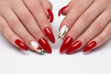 Red manicure on sharp long nails with painted anchors and umbrella on a white background. Marine...