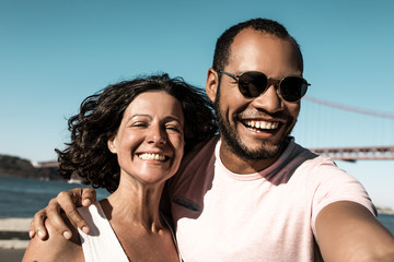 Young couple smiling at camera. Portrait of beautiful multiethnic man and woman standing together near river and smiling at camera. Emotion concept