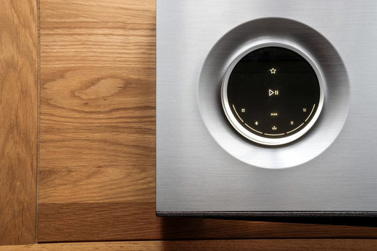 Detailed view of a luxury hi-res music streamer and smart speaker showing detail of the OLED control and large, illuminated volume dial. Seen on a hi fi cabinet.