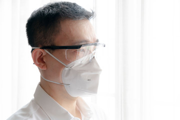 Asian man wearing safety google and N95 surgical mask to protect virus and COVID-19. Stay home,...