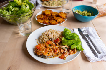 top view of healthy, fresh, organic homemade table spread with cooked salmon, green salad, guacamole, , rice and fried platano on wooden table with natural light