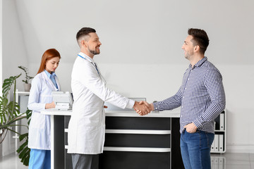 Male doctor and patient shaking hands in clinic