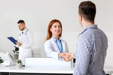 Female medical assistant and patient shaking hands in clinic