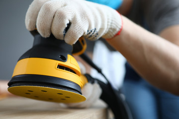 Close-up of persons hands polishing ground with grinding machine. Bright yellow sander instrument and craftsman on construction site. Protective gloves for work. Renovation concept