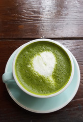 Matcha green tea latte with heart shape of decoration milk in white mug on wooden desk table at loft style coffee shop, commercial advertisement backgrounds