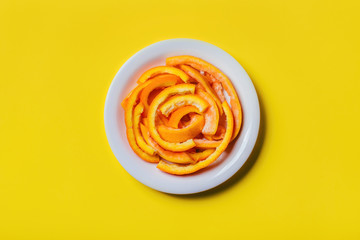 Citrus orange peels on a plate on yellow background.