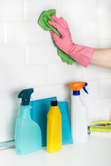 Mano con guante de látex rosa limpiando azulejos blancos junto a productos de limpieza. Vista de frente y de cerca. Copy space