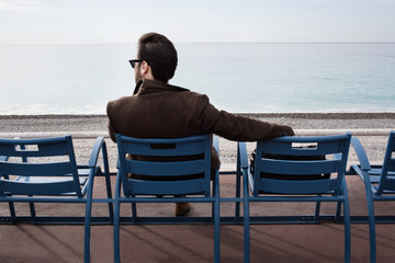 Outdoor shot of a young bearded man sitting on the bench in the bay enjoying a nice view.
