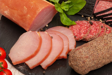 abstract background with smoked sausage with sauce, cherry tomatoes and basil on a black graphite...