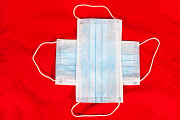 Two medical masks for one-use are on red background, laying in cross