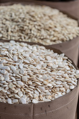 Pile of white pumpkin seeds in brown wooden bowl at food marketplace, blurred pumpkin seeds on foreground