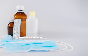 Medical banner of face masks, a thermometer for measuring body temperature, glass bottles and medicines on a gray background, front view
