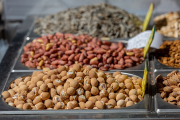 Variety of nuts in tray at food market on sunlight, macadamia nuts in focus on foreground, blurred pistachio on foreground 