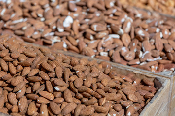 Clump of almond in tray on sunlight at food market, selective focus on foreground, blurred nuts on background
