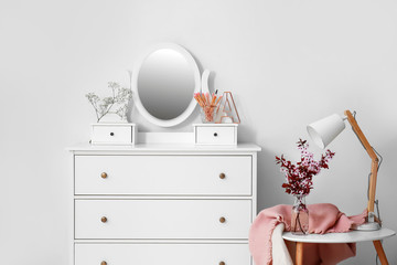 Chest of drawers with mirror and spring flowers on table in room