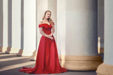 Beautiful blonde girl in a red long dress on a background of architecture, columns 