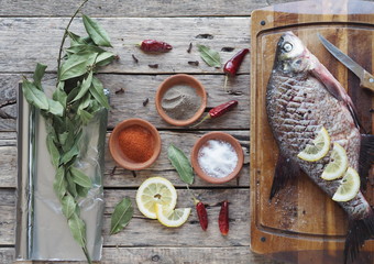 Raw river bream fish, prepared for baking in the oven with lemon slices and seasoning on a wooden board. Top view.
