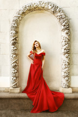 Beautiful blonde girl in a red long dress on a background of architecture, columns 
