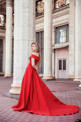 Beautiful blonde girl in a red long dress on a background of architecture, columns 