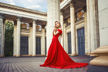 Beautiful blonde girl in a red long dress on a background of architecture, columns 