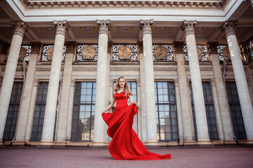 Beautiful blonde girl in a red long dress on a background of architecture, columns 