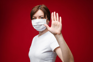 Young woman in protective suit making gesture protection by hand in glove medium close up. Portrait of female in medical safety respirator and uniform posing isolated at blue studio background