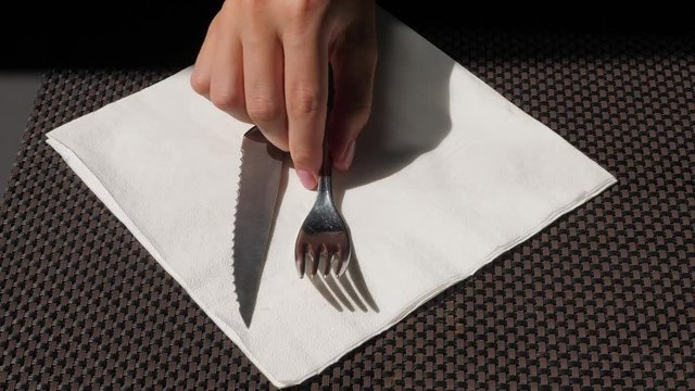 Woman tap fork by white paper napkin lying on the table, waiting for meal at cheap cafe. Closeup shot of flatware and girl hand, hungry person fiddle with fork