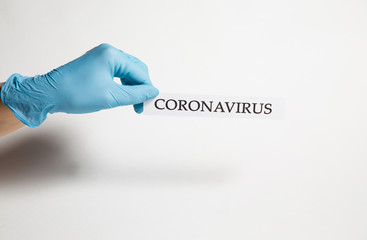A hand in a medical glove holds the inscription coronavirus on a white background - 334973882