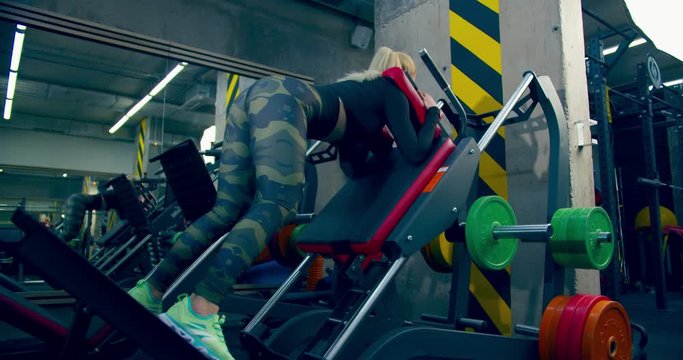 Athlete girl is playing sports in the gym with leg press machine back down view
