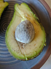 Two halves of green avocado with bone on a plate. Close-up. Background.