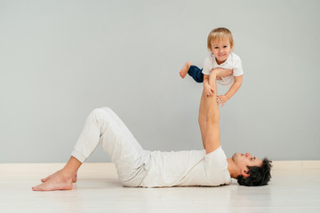 Happy loving father lying on a floor of an apartment, lifting his baby in the air. Smiling, laughing.