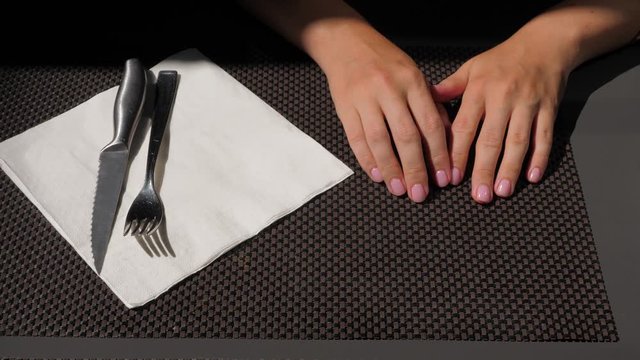 Hungry woman wait for meal at cafe, tap fingers by table. Close shot of hands, flatware lie near on paper napkin, stainless steel steak knife and fork. Lady bored of waiting for long time