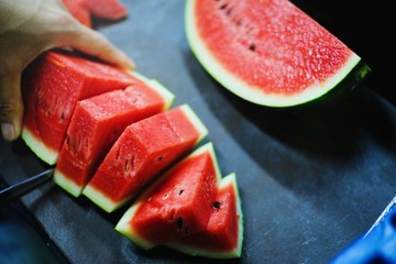 Hand holding red watermelon And use a knife to cutting watermelon in pieces to fruit plate.