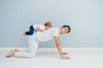 Fototapeta na wymiar A sports man is engaged in fitness and yoga with a baby at home