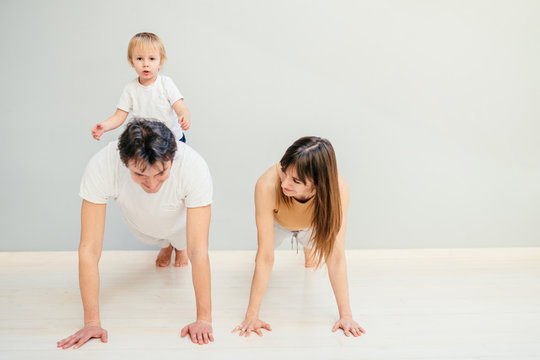 Happy Parents Dad And Mom While Their Little Son Climbing, Sitting On Daddy's Back. Sport, Active Lifestyle, Family Relations Concept.