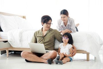 Asian family using notebook in bedroom. Father works with a notebook. With a mother and child to support