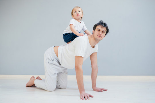 Father working out, doing single arm plank with his jolly infant baby riding on his neck. At home apartment.