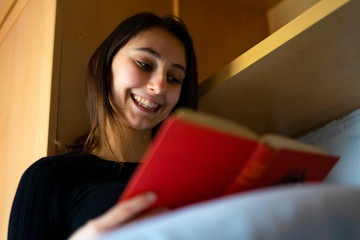 Naklejka premium Young woman reading a red book in bed.