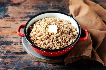 Boiled buckwheat with butter in a pan on a dark wooden background