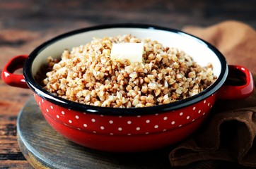 Boiled buckwheat with butter in a pan on a dark wooden background
