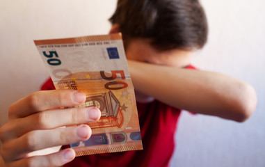 Teen guy holds out his hand with a 50 Euro bill on a light background