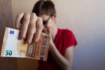 Teen guy holds out his hand with a 50 Euro bill on a light background
