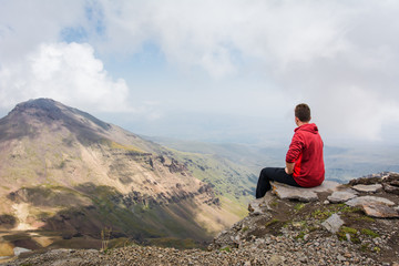 Fototapeta premium Young man sitting and looking around beautiful panoramic landscape of Mount Aragats mountain in Armenia