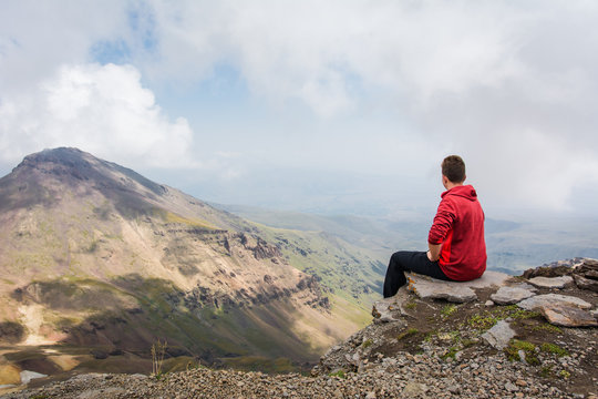 Young man sitting and looking around beautiful panoramic landscape of Mount Aragats mountain in Armenia