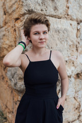 a girl with short hair in a black summer dress is sitting on the rocks